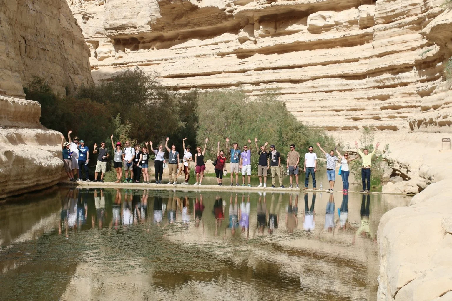 A group of people standing spread out across a body of water, infront of a rock formation